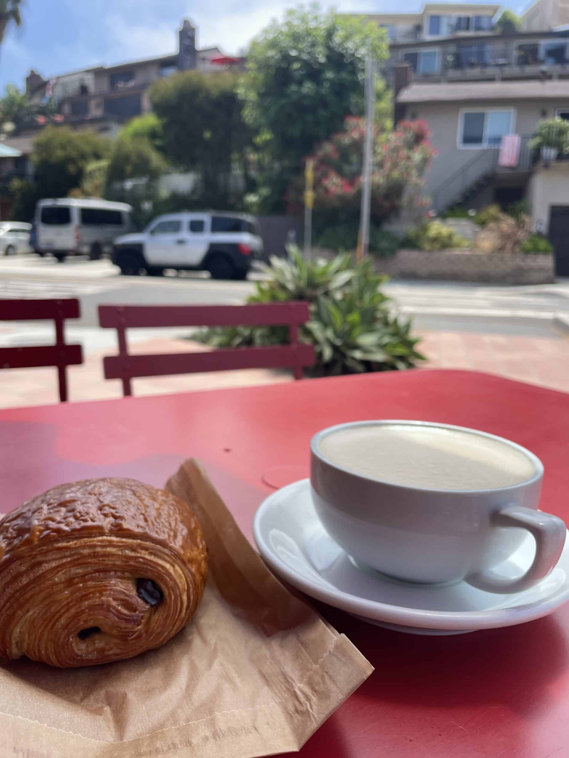 a croissant with a latte in a white mug on a red table at a coffee shop in San Clemente