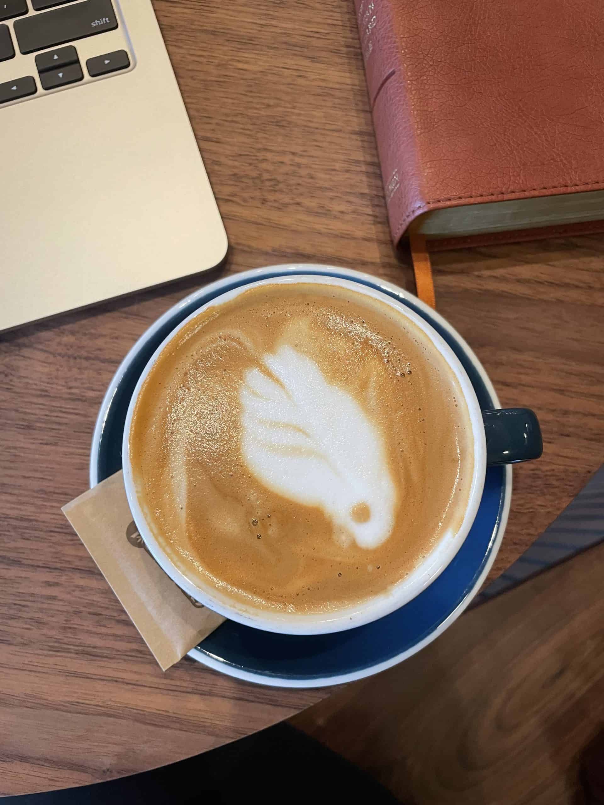 cappuccino in a navy blue mug on a dark wooden table with a bible in the corner