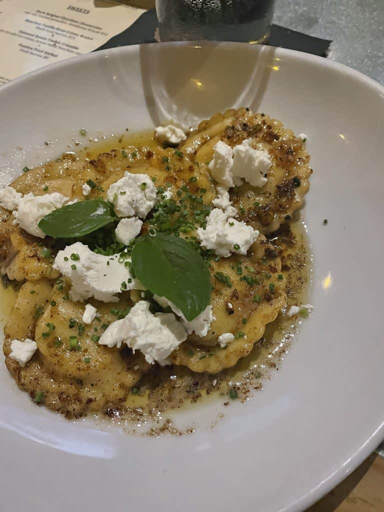 ravioli with goat cheese and basil on top inside of a white bowl