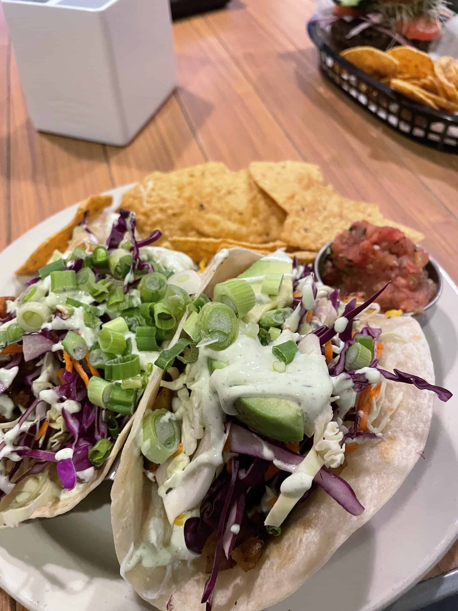 two flour tortillas filled with avocado, green onions, cabbage, potatoes and a white cream sauce on top with chips and salsa on the side