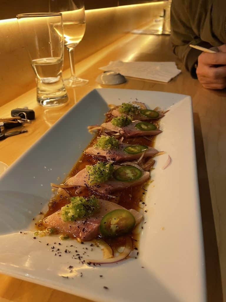 yellowtail sashimi on a plate with sliced jalapeño and chopped onions on top