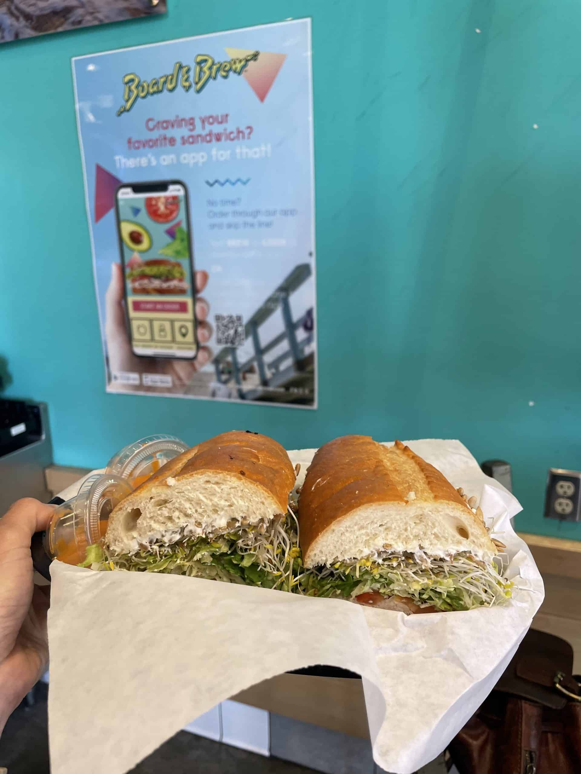 a turkey sandwich in a plastic bowl with white paper held up against a teal blue wall