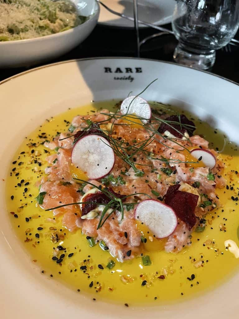 salmon tar tar with sliced radishes on top of a yellow sauce