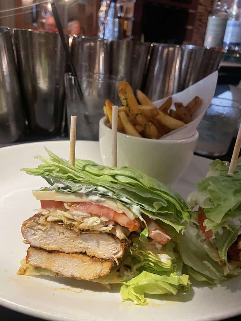 a grilled chicken burger with a lettuce bun, tomatoes and cheese with french fries in the background