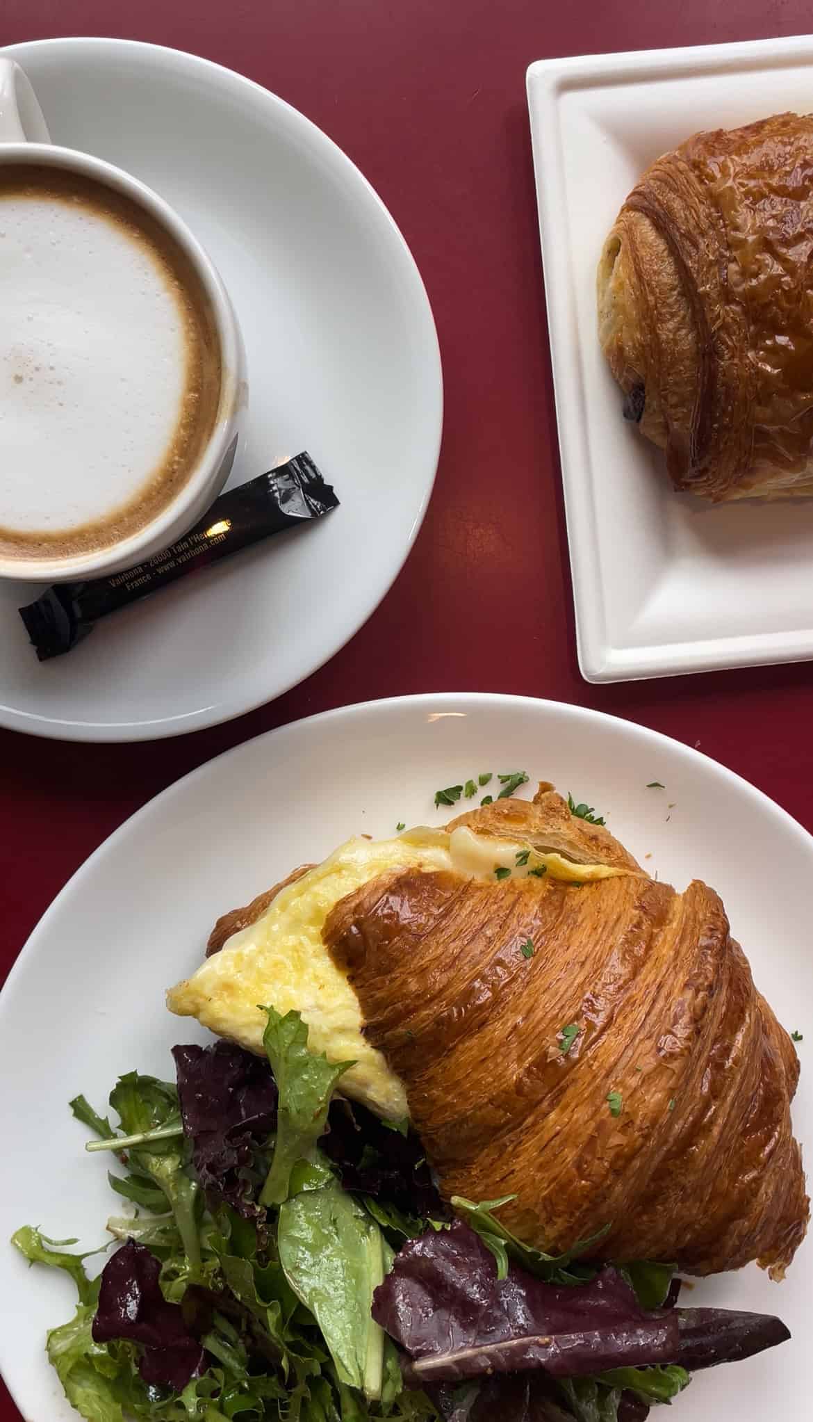 a croissant sandwich with a salad on the side and a chocolate croissant on a separate plate