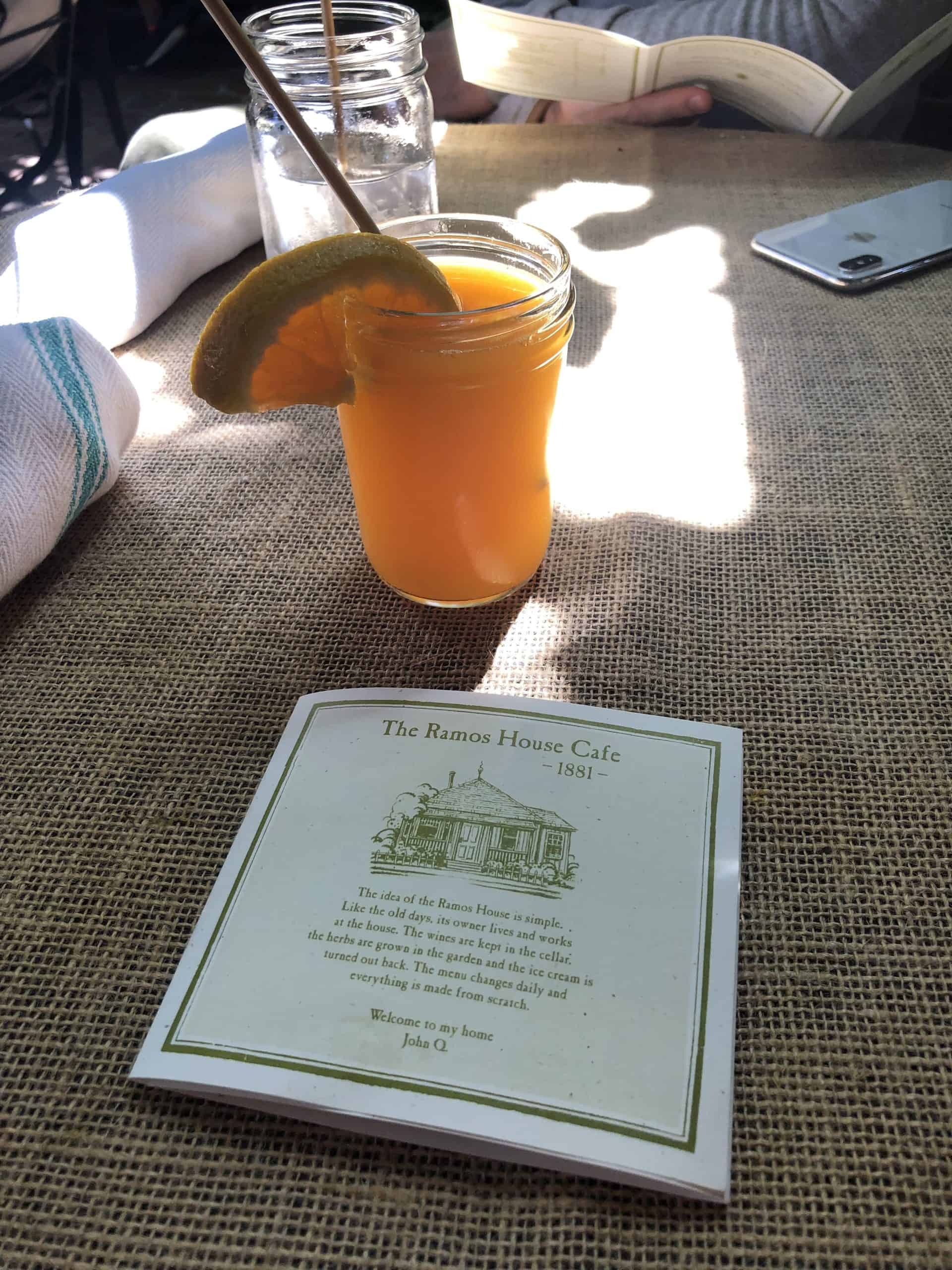 orange juice in a mason jar cup with The Ramos House Cafe menu on a table