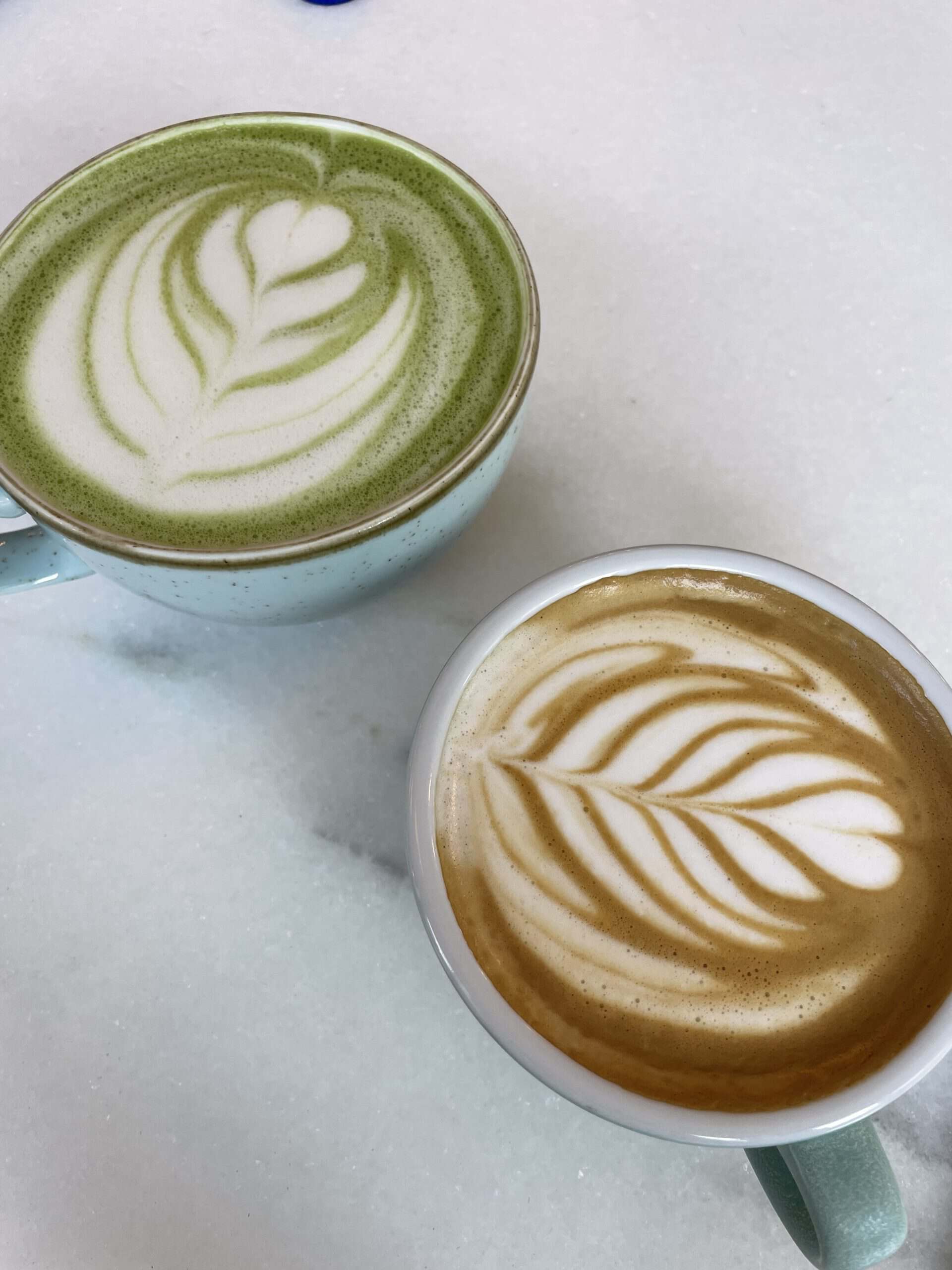 a matcha latte and cappuccino on a white marble table
