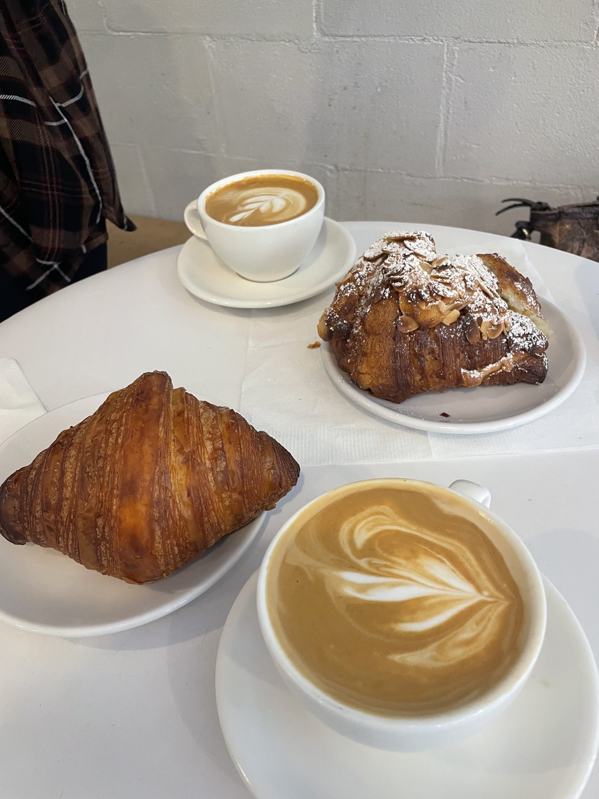 two cappuccinos in white ceramic cups with a plain and almond croissant