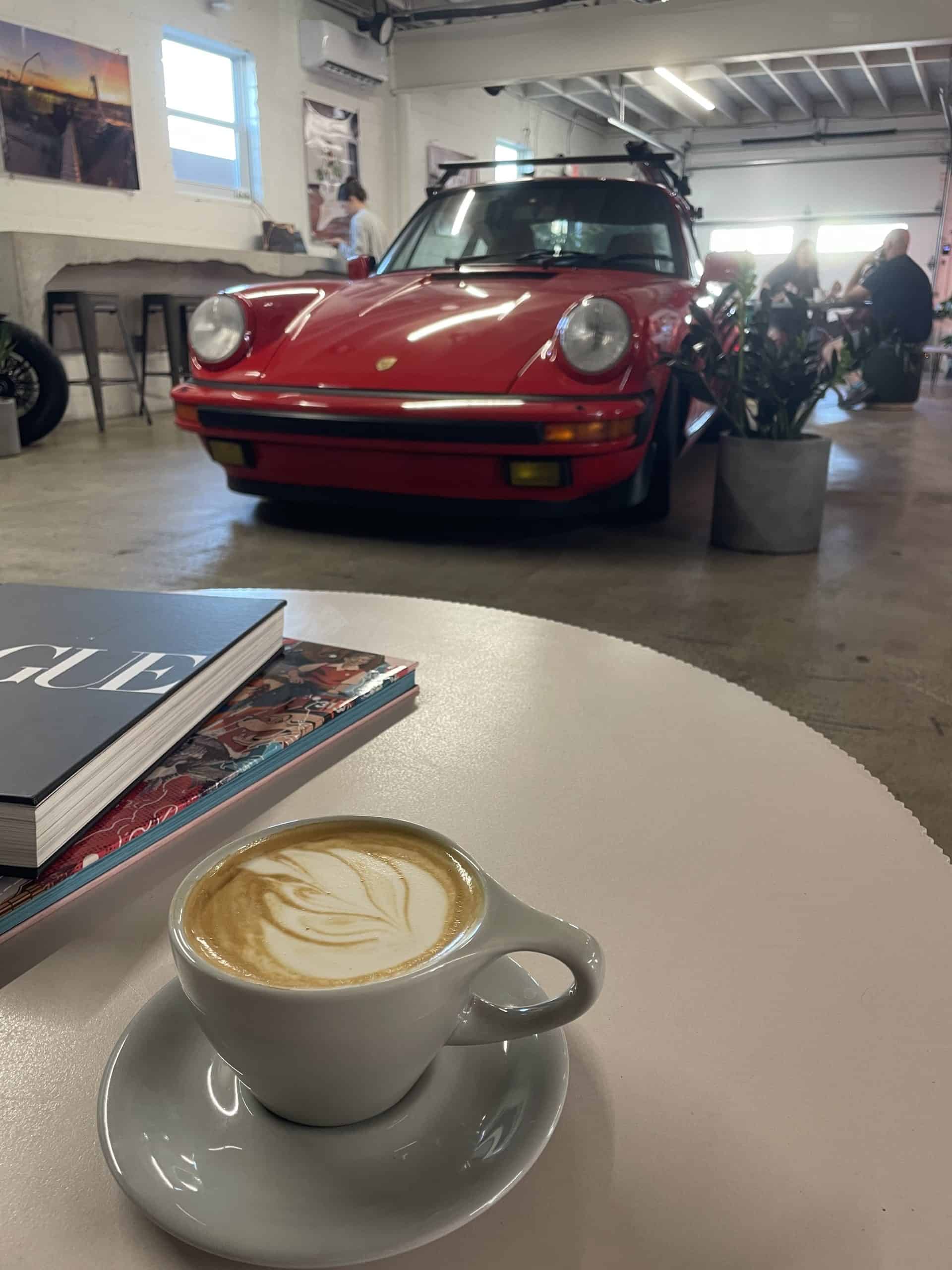 a latte in a grey ceramic cup with an old red Porsche behind it